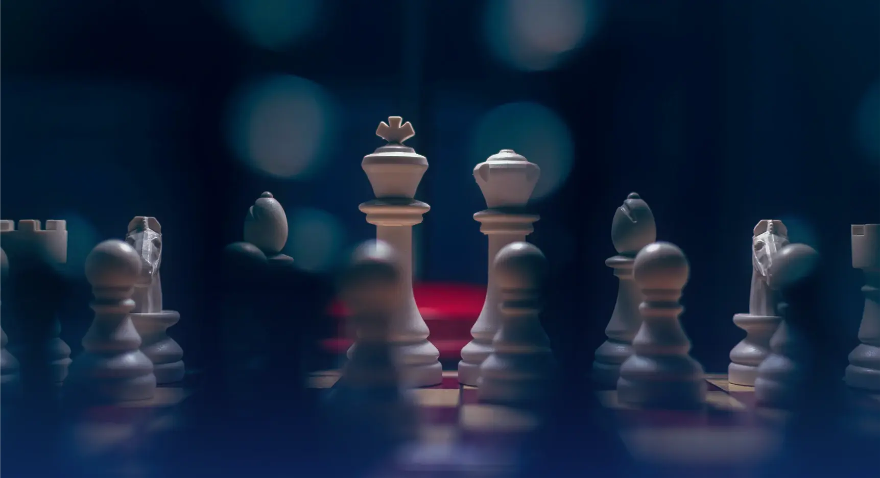 Primer plano de piezas de ajedrez blancas en un tablero iluminado con fondo oscuro.