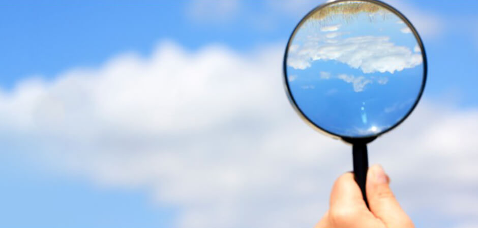 Mano sosteniendo una lupa enfocando las nubes en el cielo