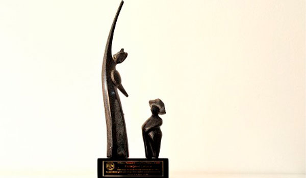 Estatuilla de bronce con figuras estilizadas sobre base con placa de reconocimiento.